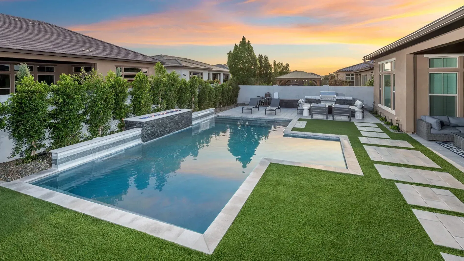 Backyard with pool, outdoor dining area, and houses at sunset.