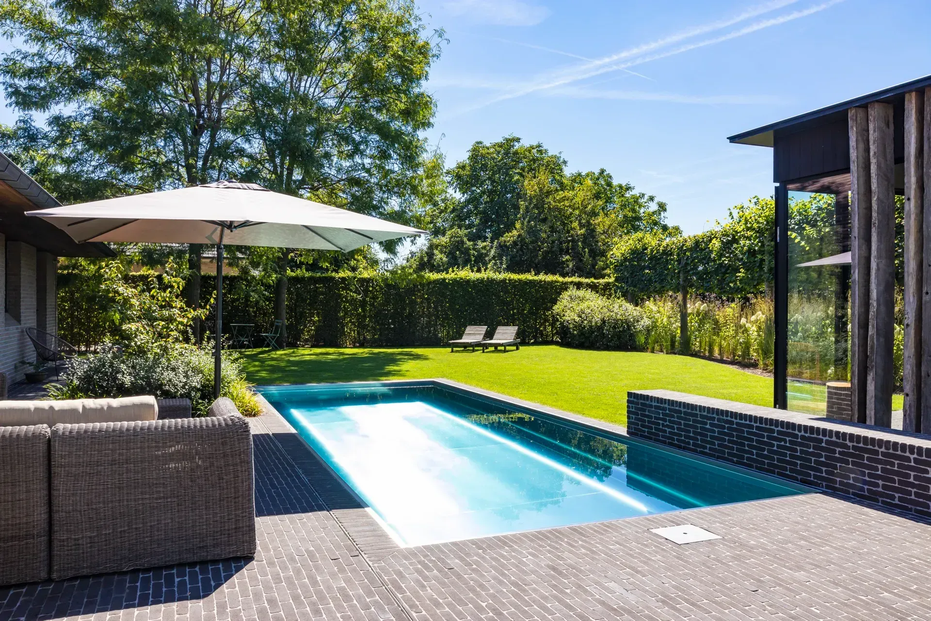 Pool and patio area with umbrella, lounge chairs, and a green lawn. Sunny day.