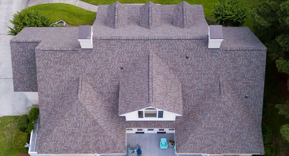 Person installing red roof shingles with a nail gun on a sunny day.