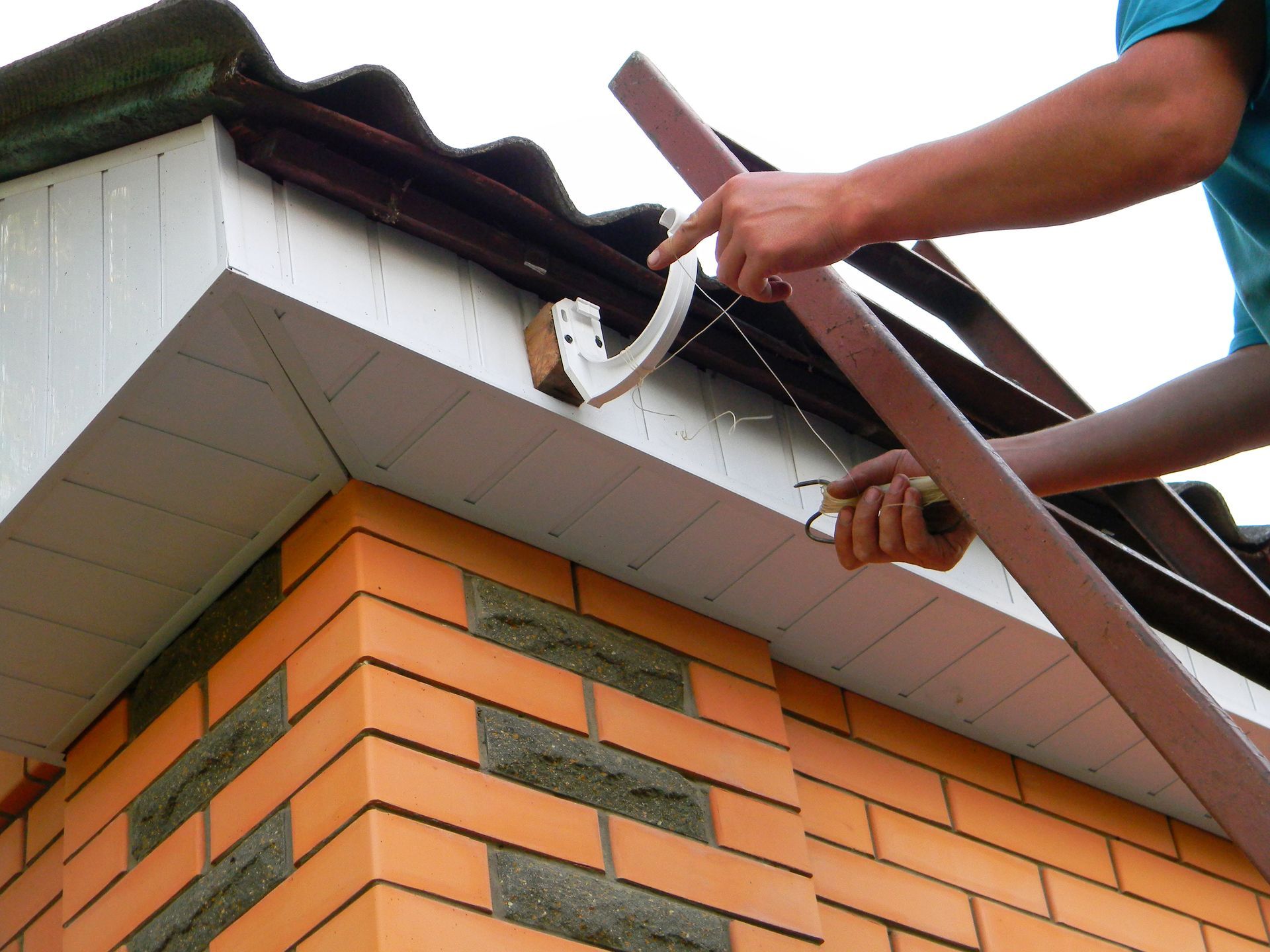 Person installing a brown gutter bracket on a brick building's roof.
