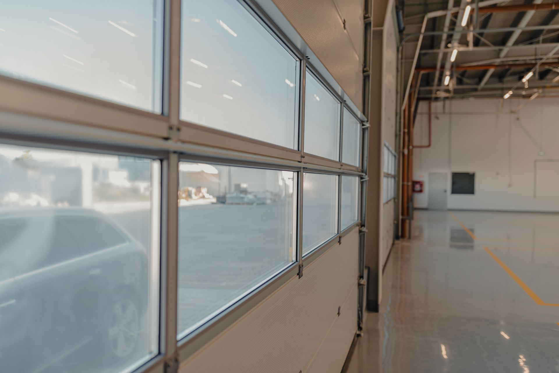 Partially open industrial garage door with glass panes, interior view. Sunlight, concrete floor, interior of warehouse.