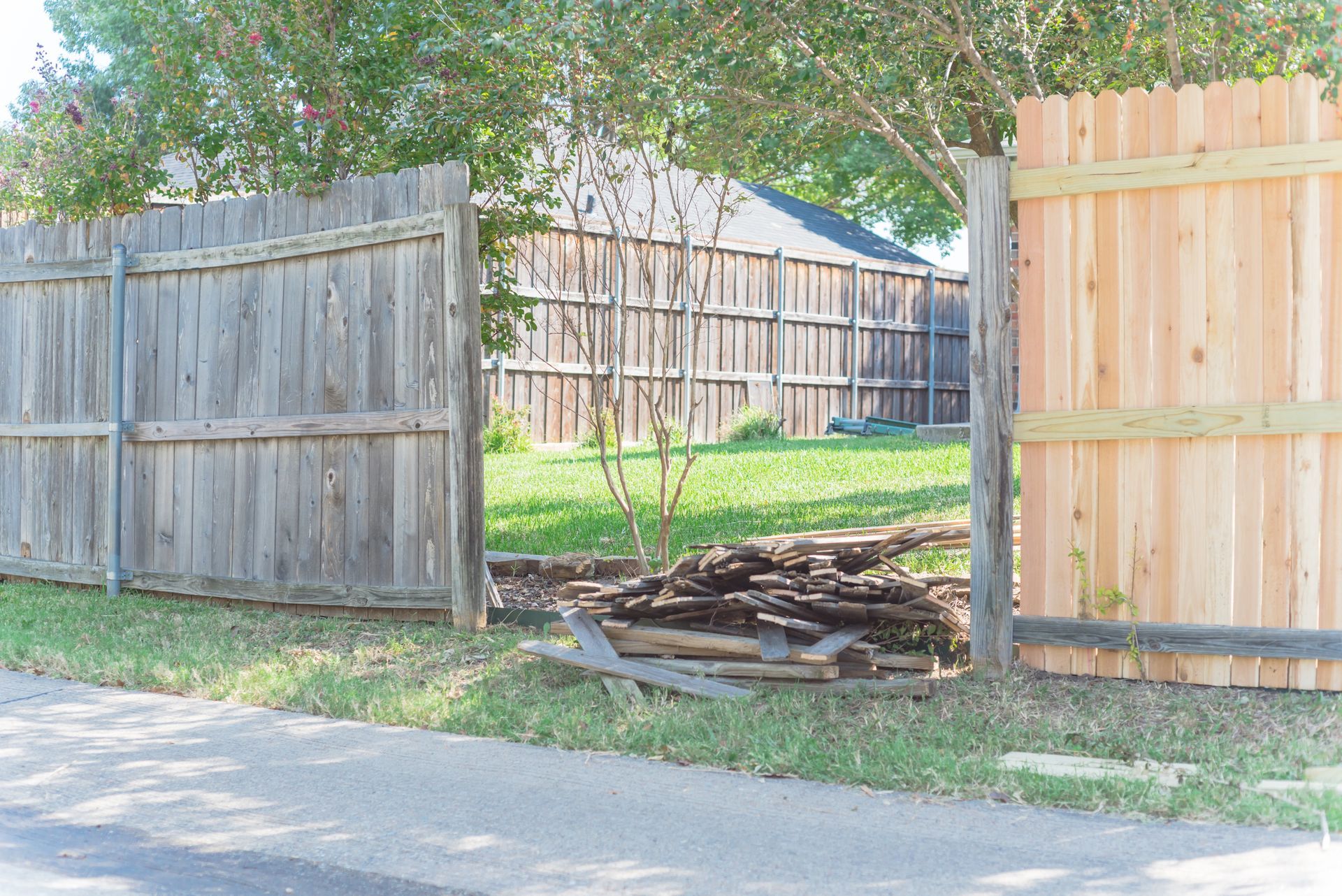Person using a power drill to attach a wooden fence post. The scene is outdoors, sunny.