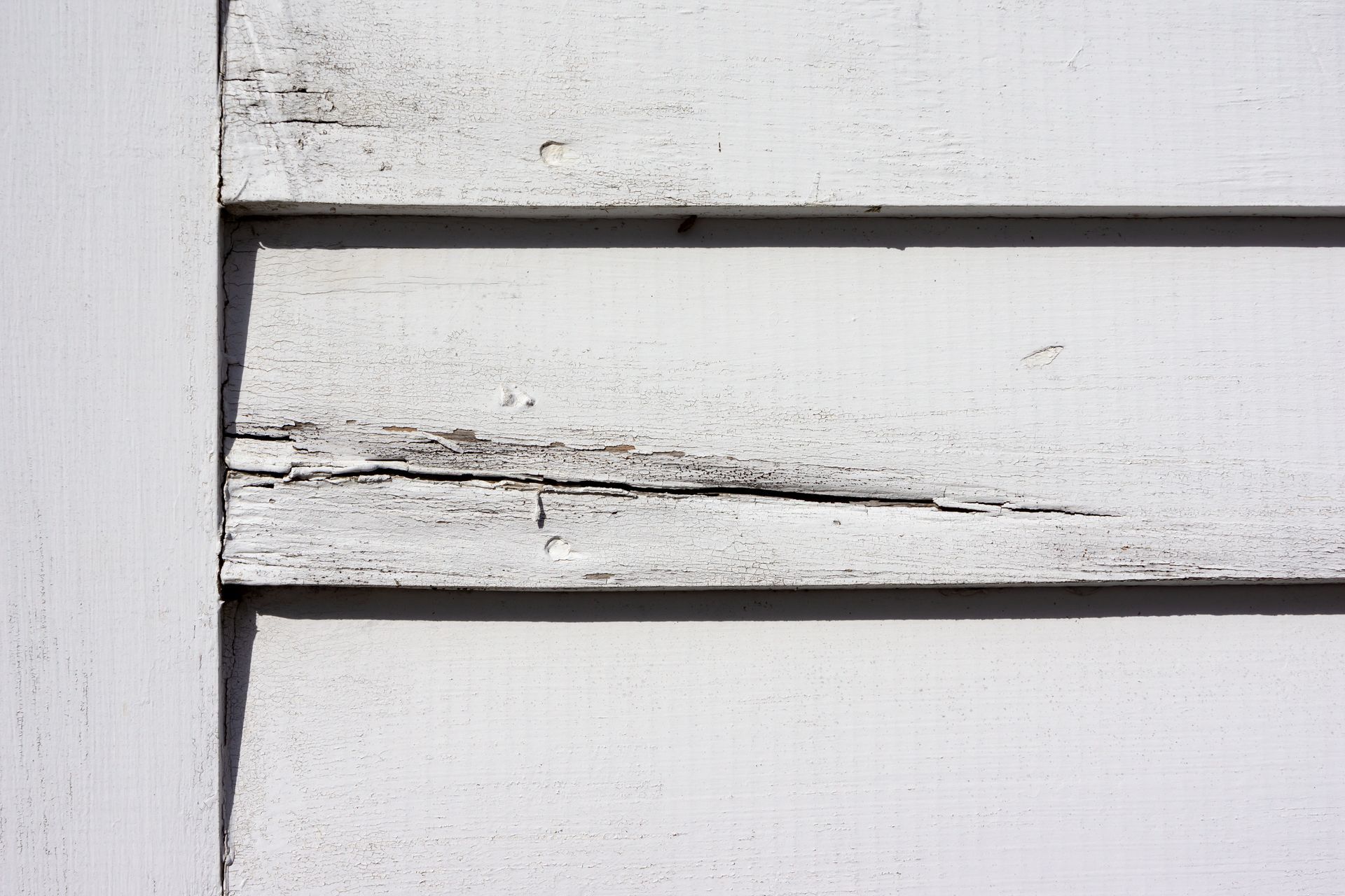 Close-up of weathered white clapboard siding with peeling paint and a visible crack.