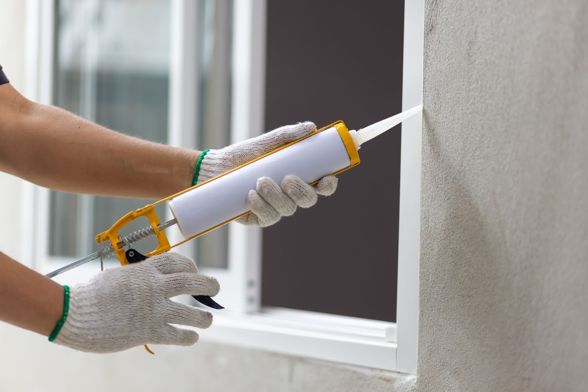 Person applying caulk to a window frame with a caulk gun.