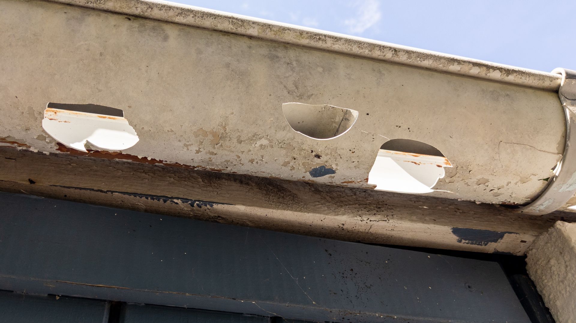 Damaged white rain gutter with multiple holes.