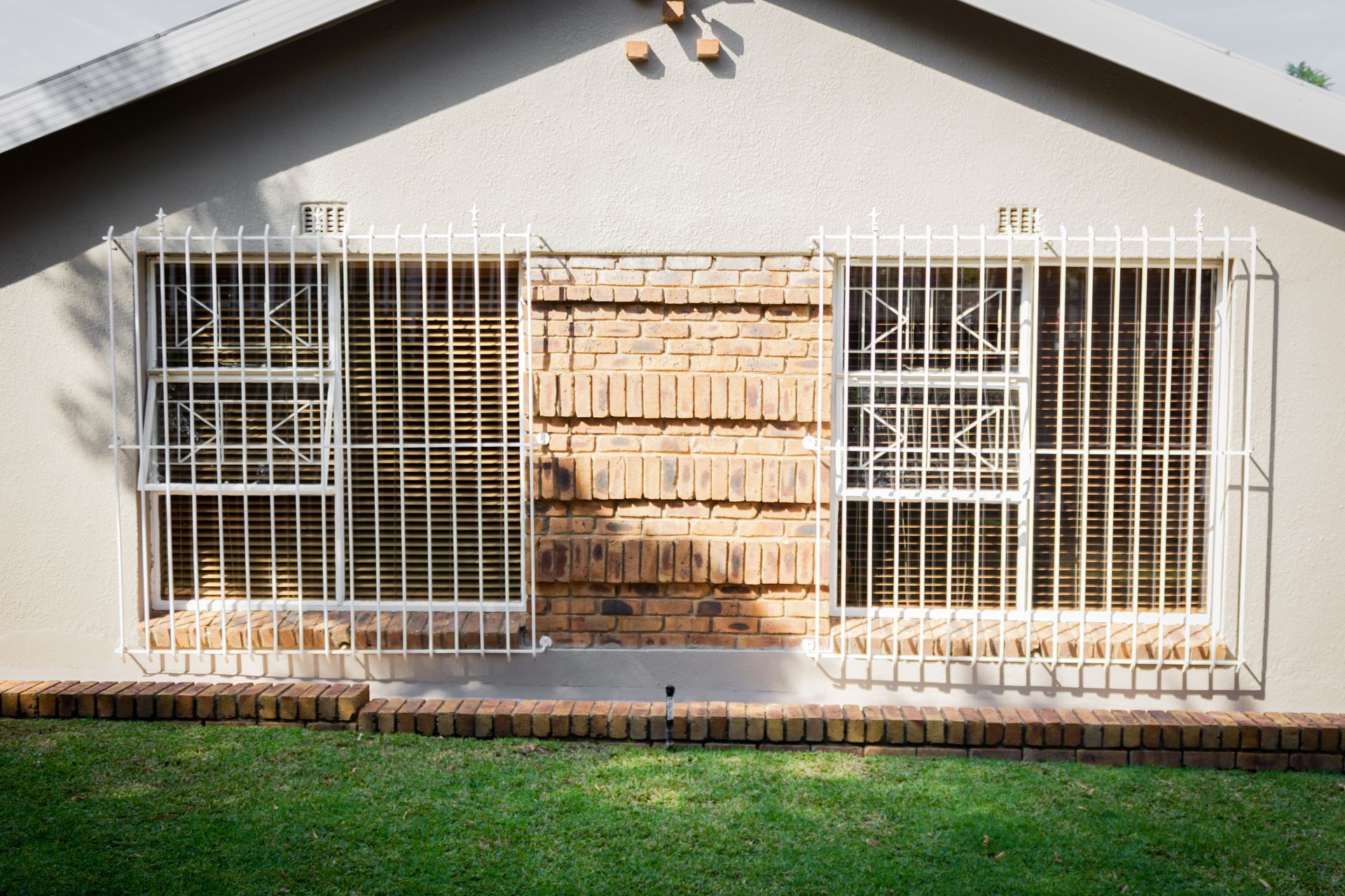 Exterior of a house with barred windows. Center window is bricked up; a green lawn is in front.