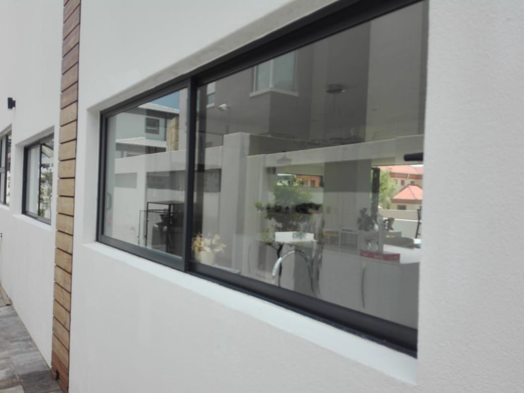 Black-framed sliding window on a white building reflecting a room with bright light.