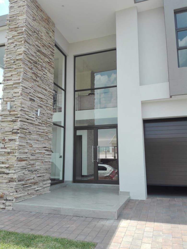 Modern home exterior with stone and white facade, large windows, and a garage.