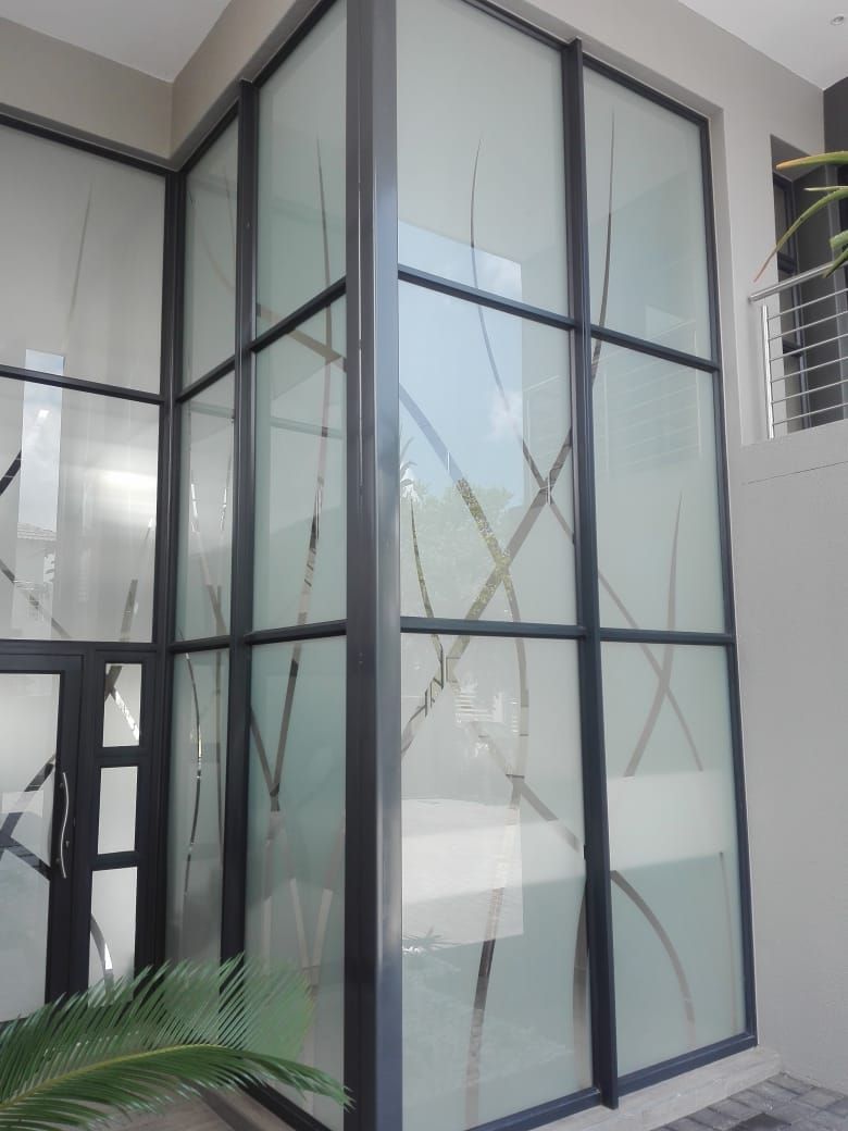 Frosted glass windows with dark frames, decorated with plant-like designs. Outdoors, modern building.