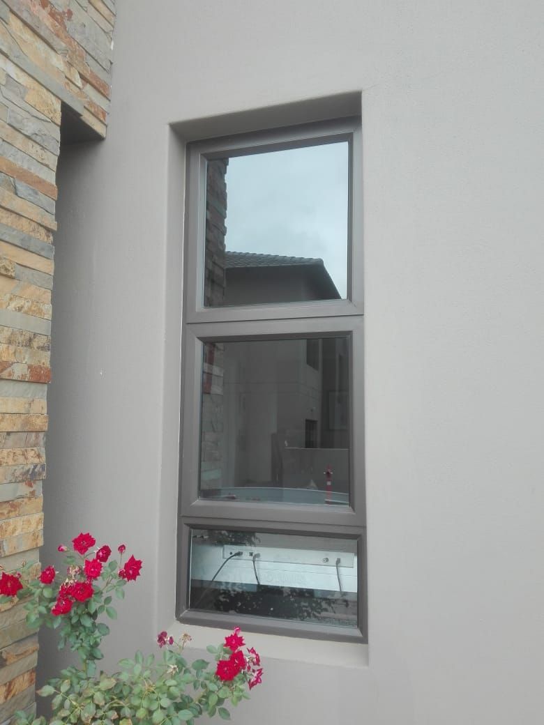 Tall, three-pane window with dark gray frame on light gray exterior wall. Red roses in foreground.