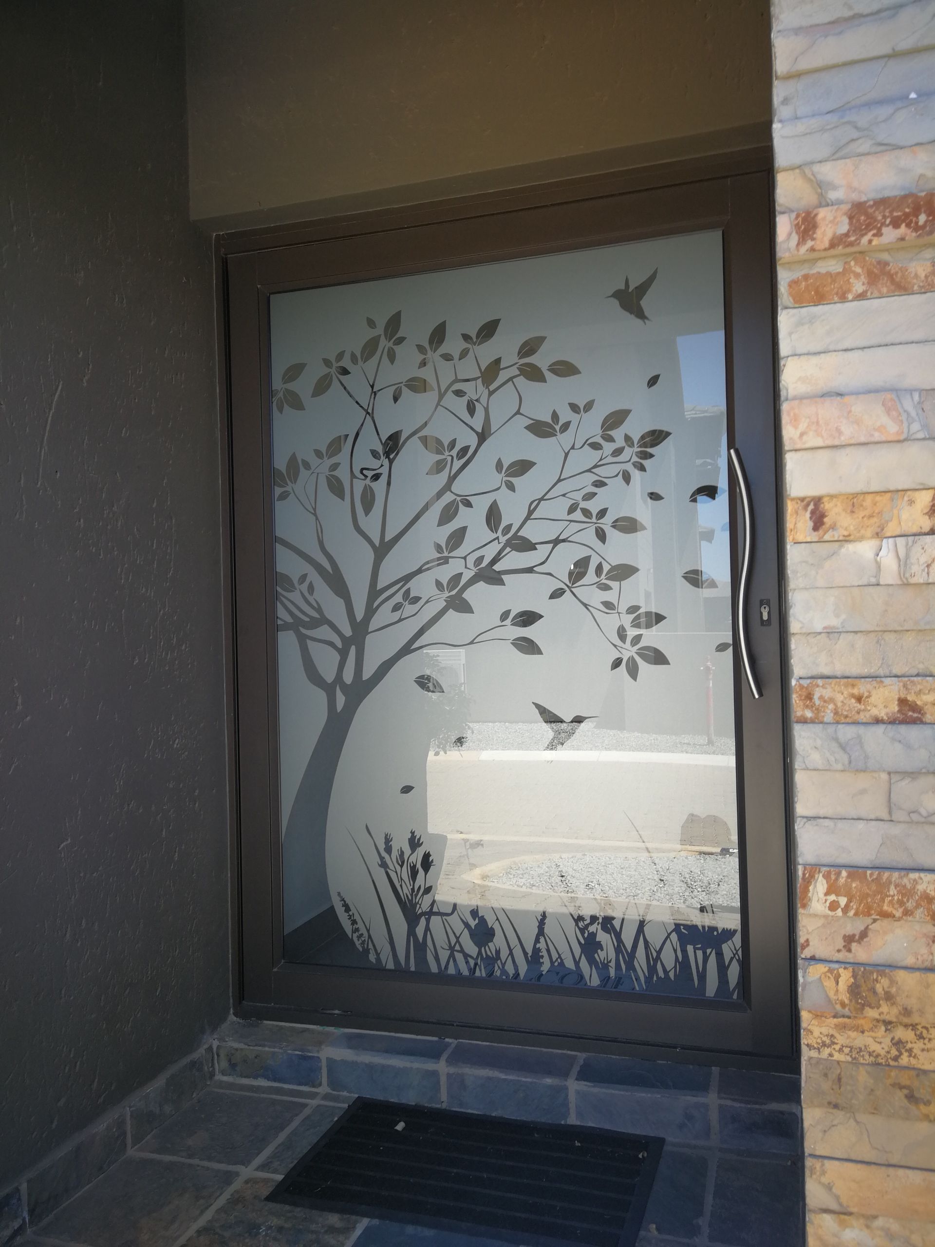 Frosted glass door with tree and birds design; in an entryway with stone and dark gray walls.