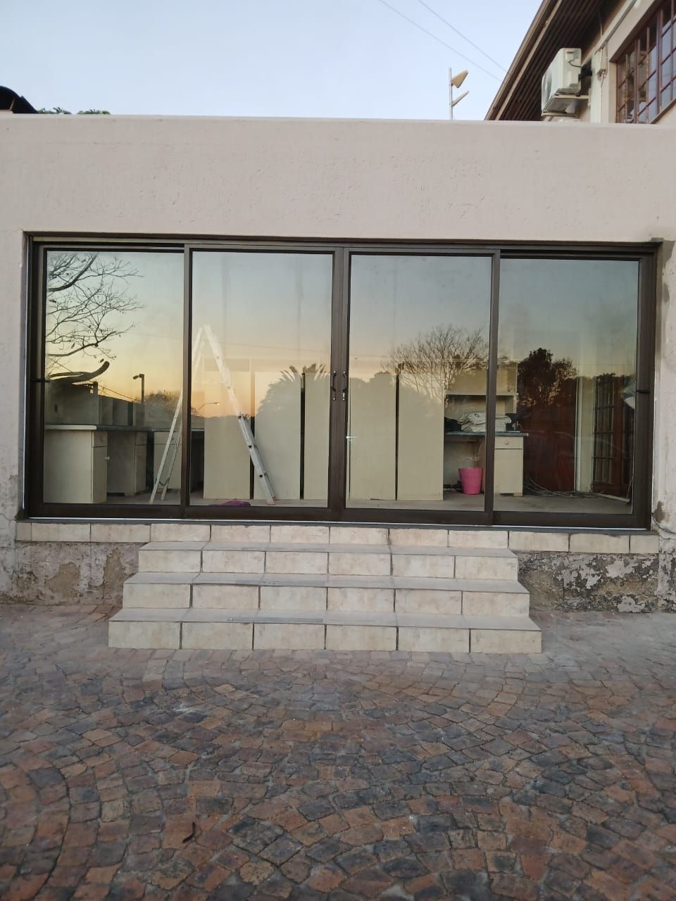 Exterior of a building with dark-framed sliding glass doors above three steps. Reflected sunset visible.