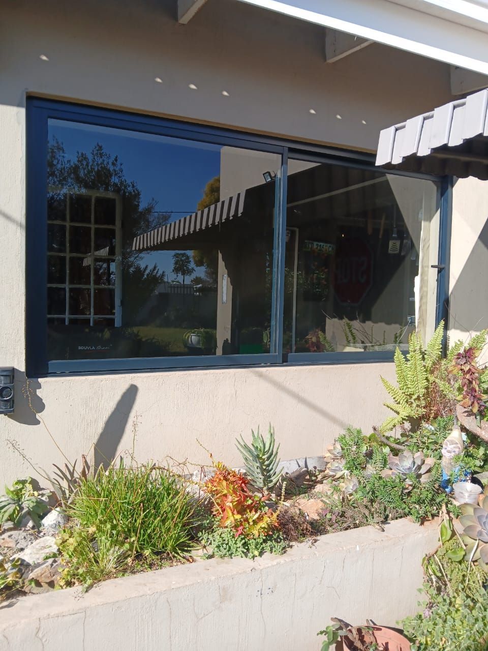Large sliding glass window with black frame reflecting an outdoor scene; flowers in a garden below.