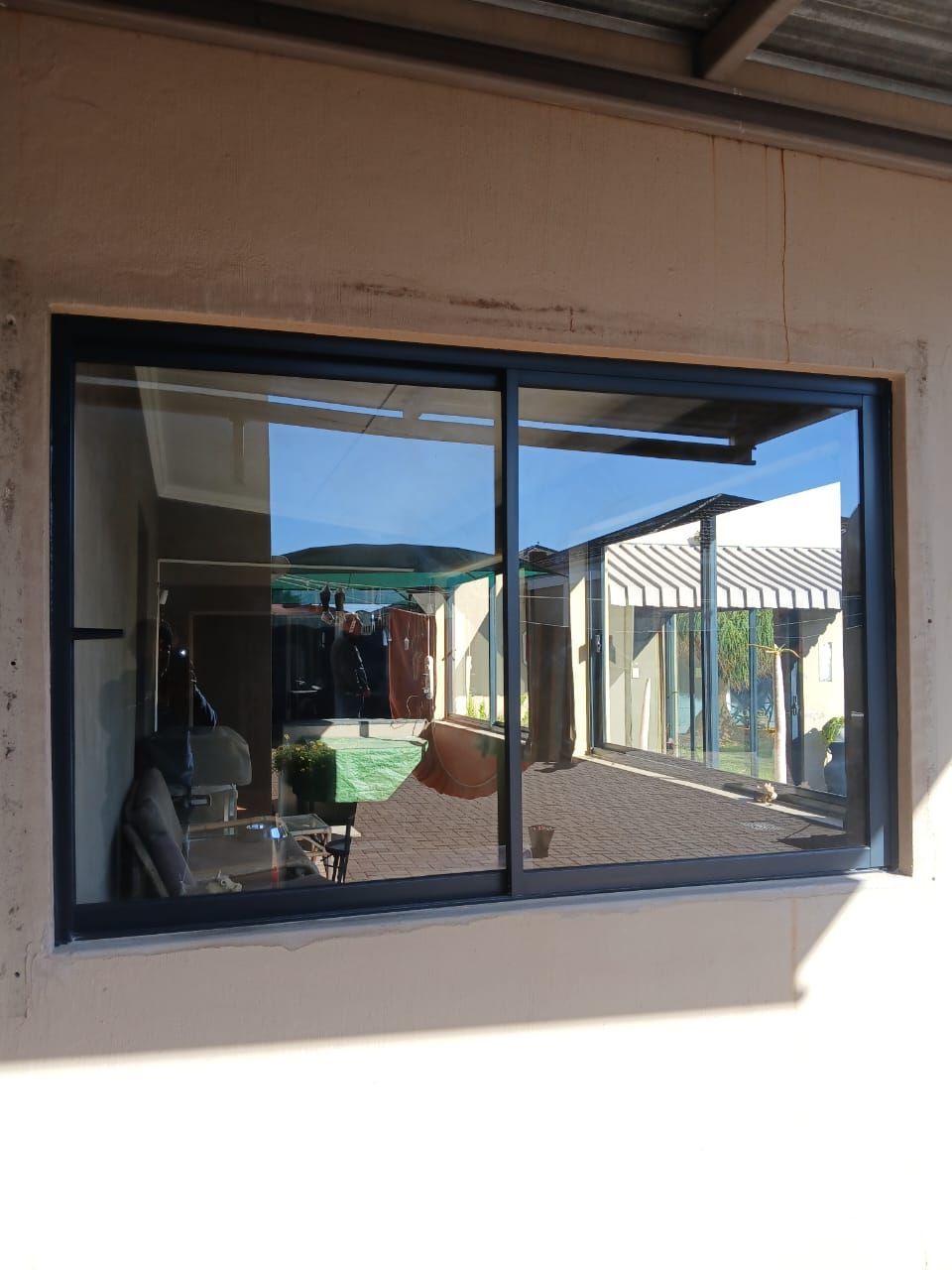 A black-framed sliding window reflecting a courtyard with buildings and objects; the wall is cream-colored.