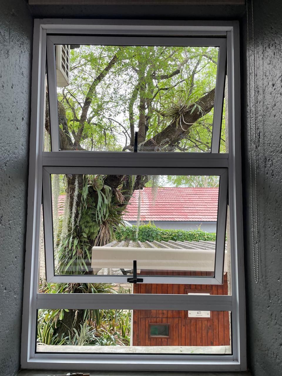 White framed window with two panes open, showing a tree and red-roofed building.
