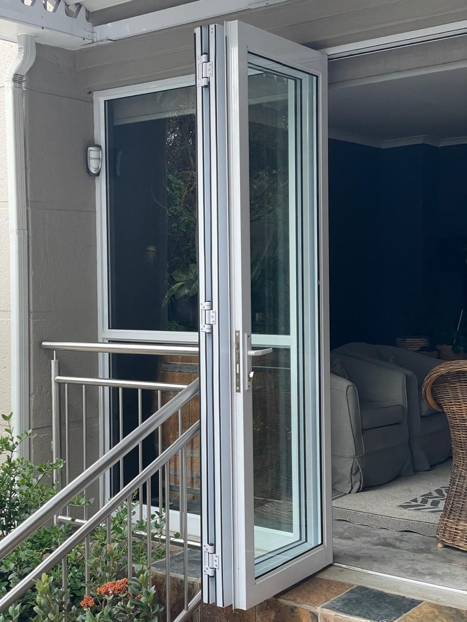 Bifold glass doors with silver frames open onto a patio. A railing and small window are also visible.