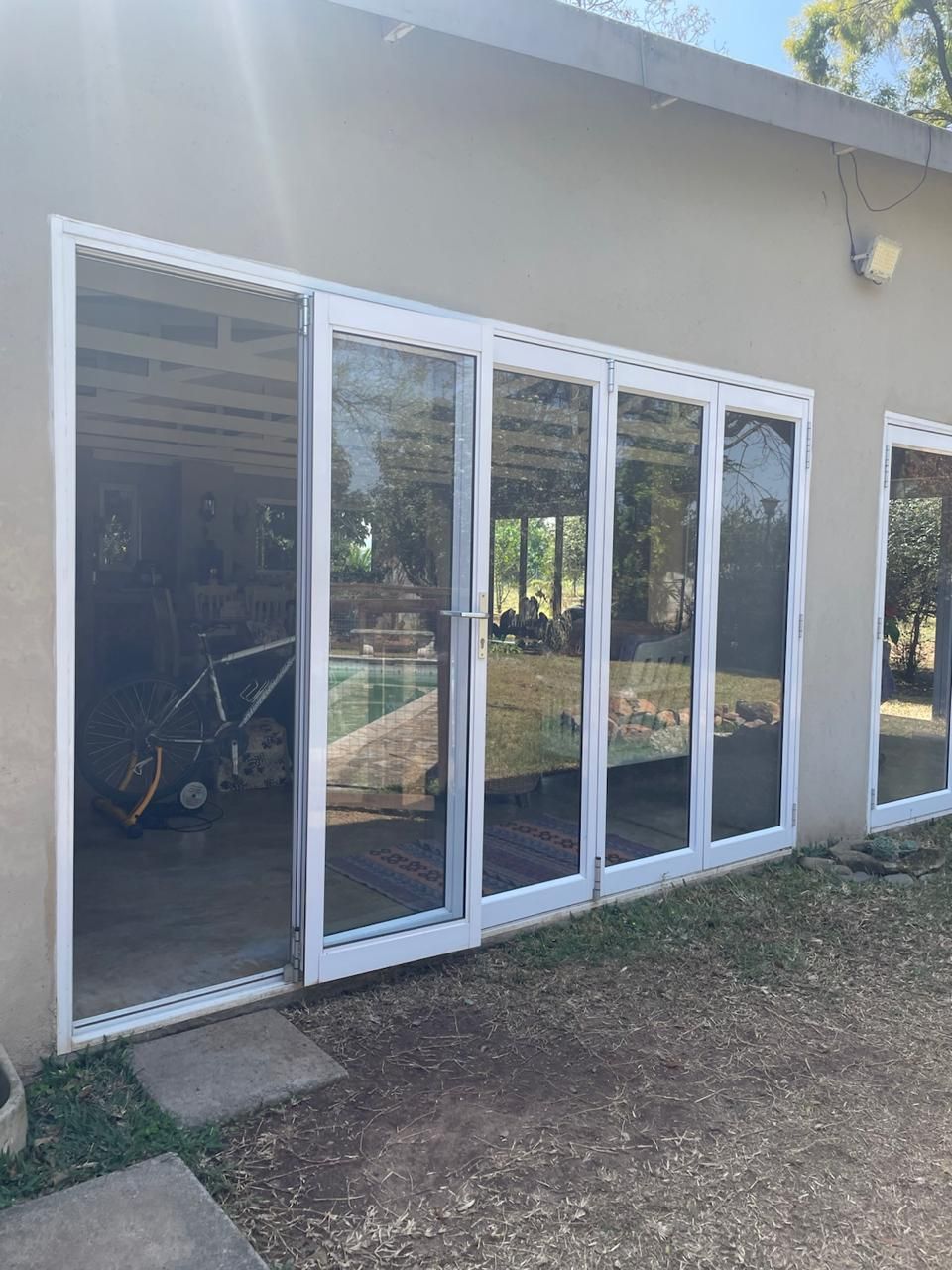 White framed glass doors, open and closed, on a light-colored building, leading to a pool area.