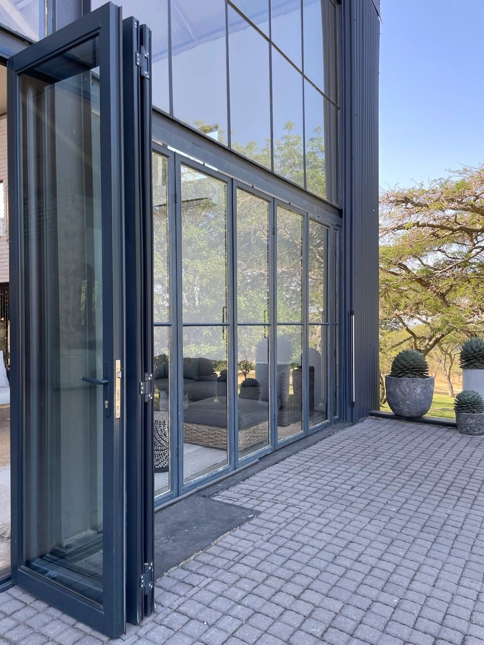 Dark gray folding glass doors open onto a paved patio, leading into a modern building with large windows.