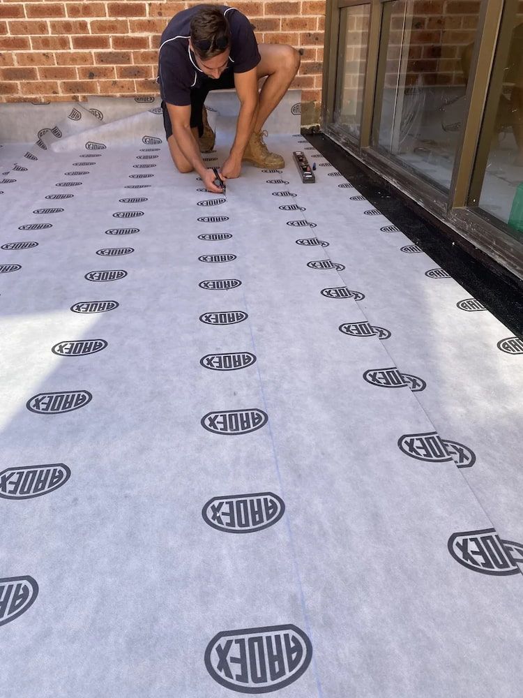 Man Kneeling, Installing Waterproof Membrane on a Patio — Unique Waterproofing Solutions in North Rocks, NSW
