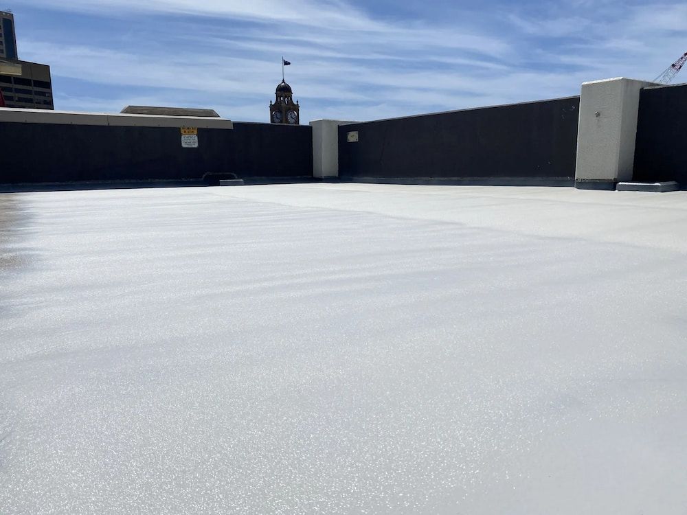 White-coated Rooftop With a City Backdrop Under a Blue Sky — Unique Waterproofing Solutions in North Rocks, NSW