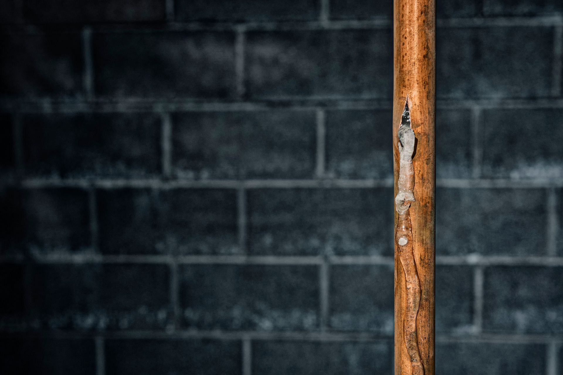 A broken, frozen copper pipe, needing insulated pipes in a basement to prevent freezing in winter.