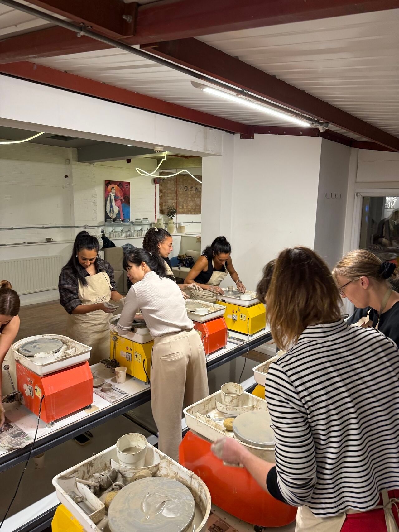 People working at pottery wheels in an indoor studio with orange equipment.