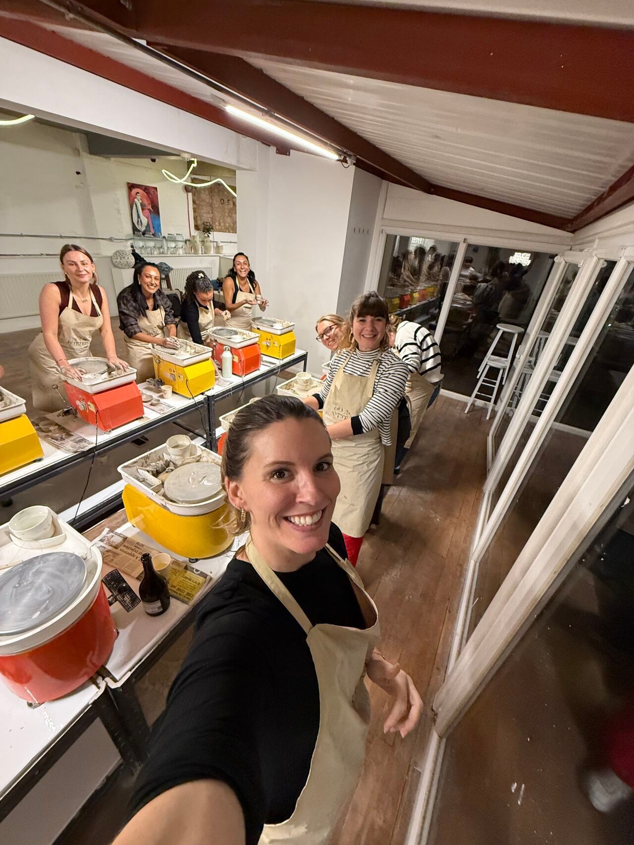 Three people talk in a brightly lit office setting, with a woman in a black blazer holding a glass while conversing.