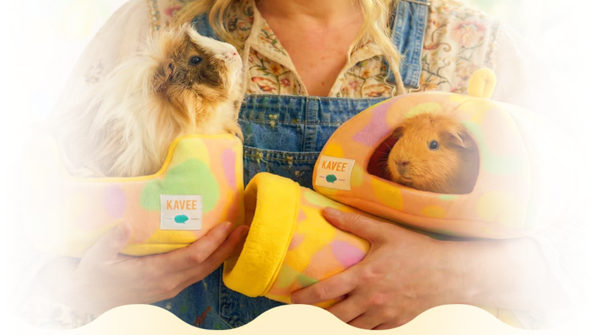 A person holds two colorful guinea pig beds, each containing a guinea pig, against a patterned background.