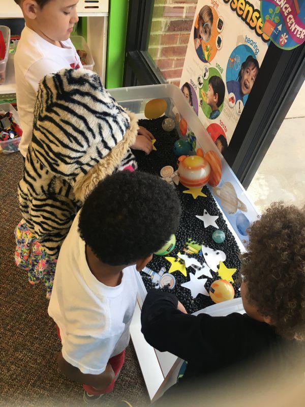 Children at a sensory table with toys. One is wearing a zebra costume. They are at the Science Center.