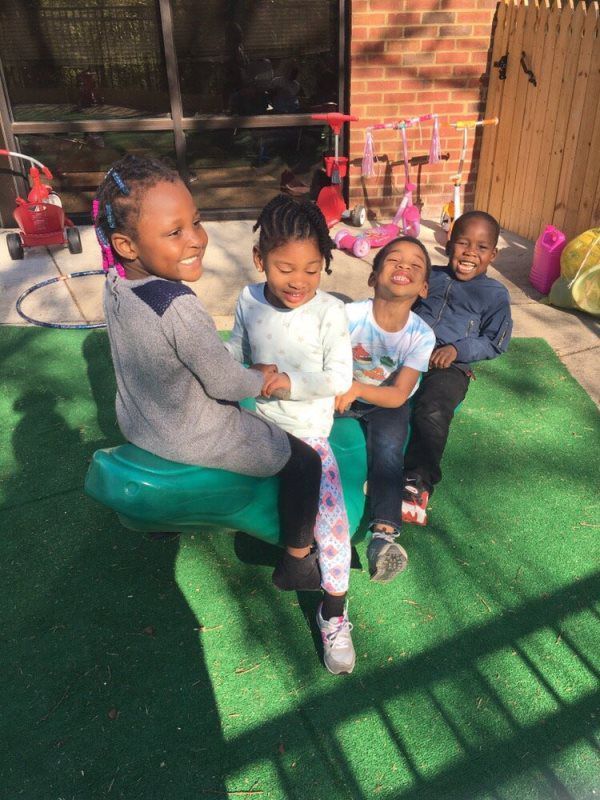 Four children laughing on a green teeter-totter outdoors.