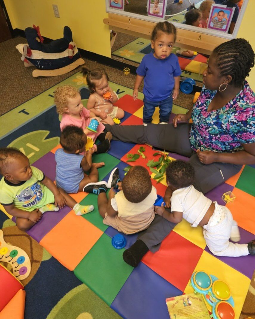 Children planting in pots outside an early learning center. A man looks over their shoulders.