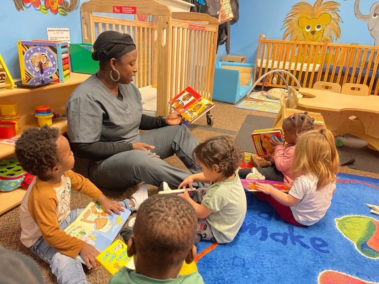 Children sitting in a circle listening to an adult. Brightly colored room, red and blue chairs.
