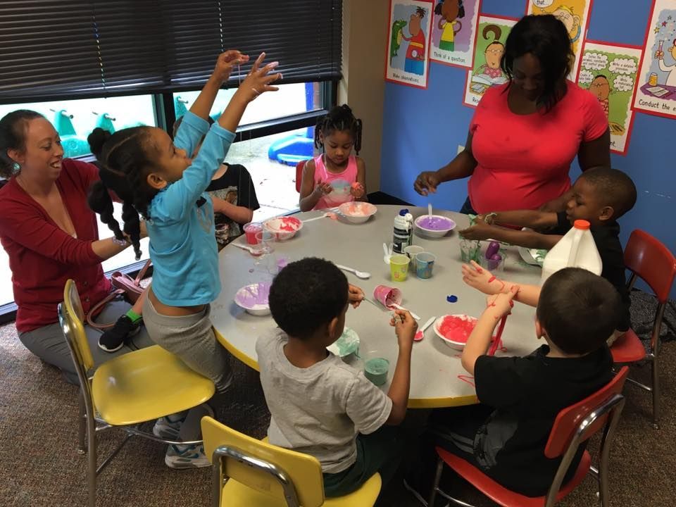 Group of children in blue shirts posing in front of a large airplane engine, with several adults.