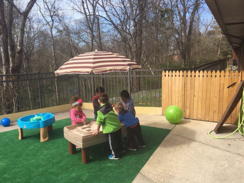 Children playing at an outdoor sand table under an umbrella.