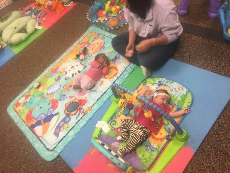 Babies laying on playmats with a person nearby. Toys scattered on the floor.