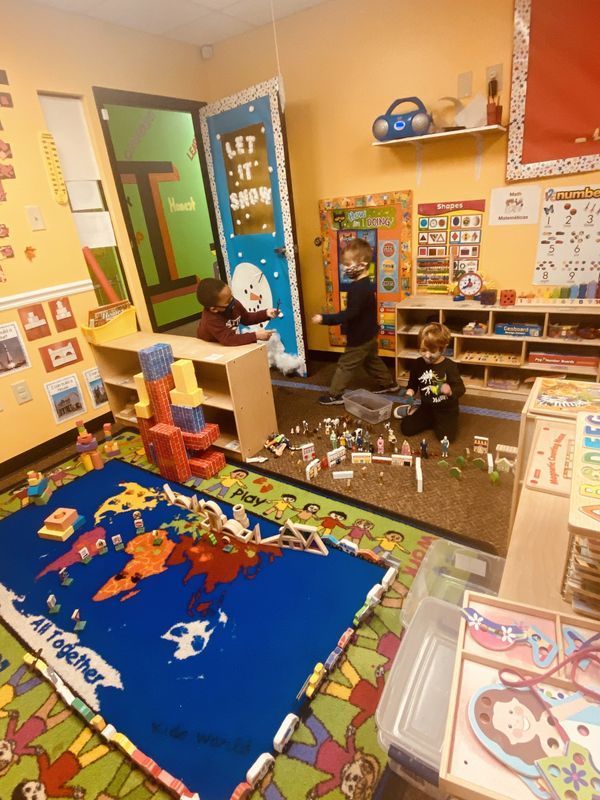 Children playing in a colorful classroom. Building blocks are scattered on a world map rug and the floor.