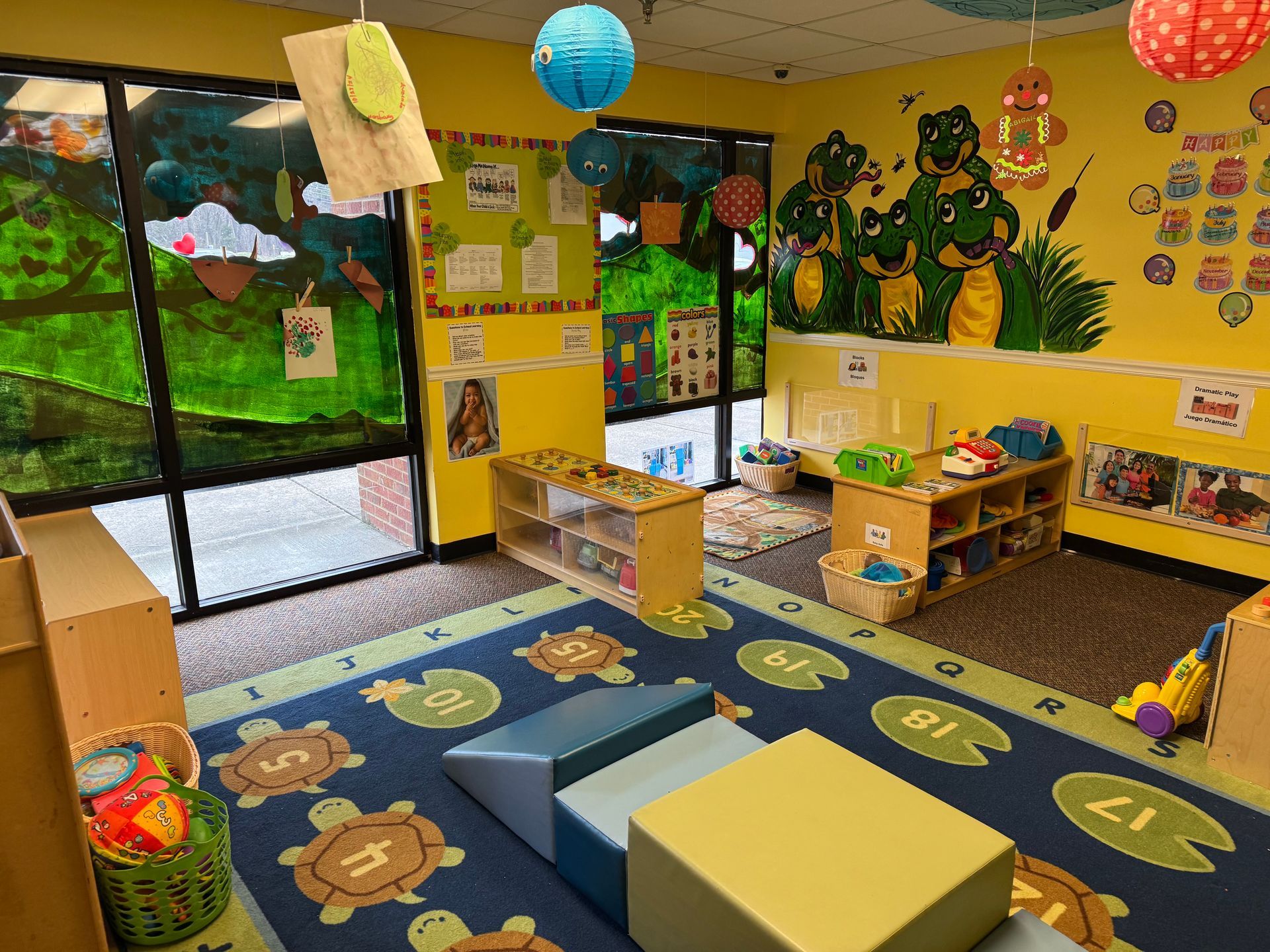 Children at a table create art with guidance from adults. Bright, colorful room.