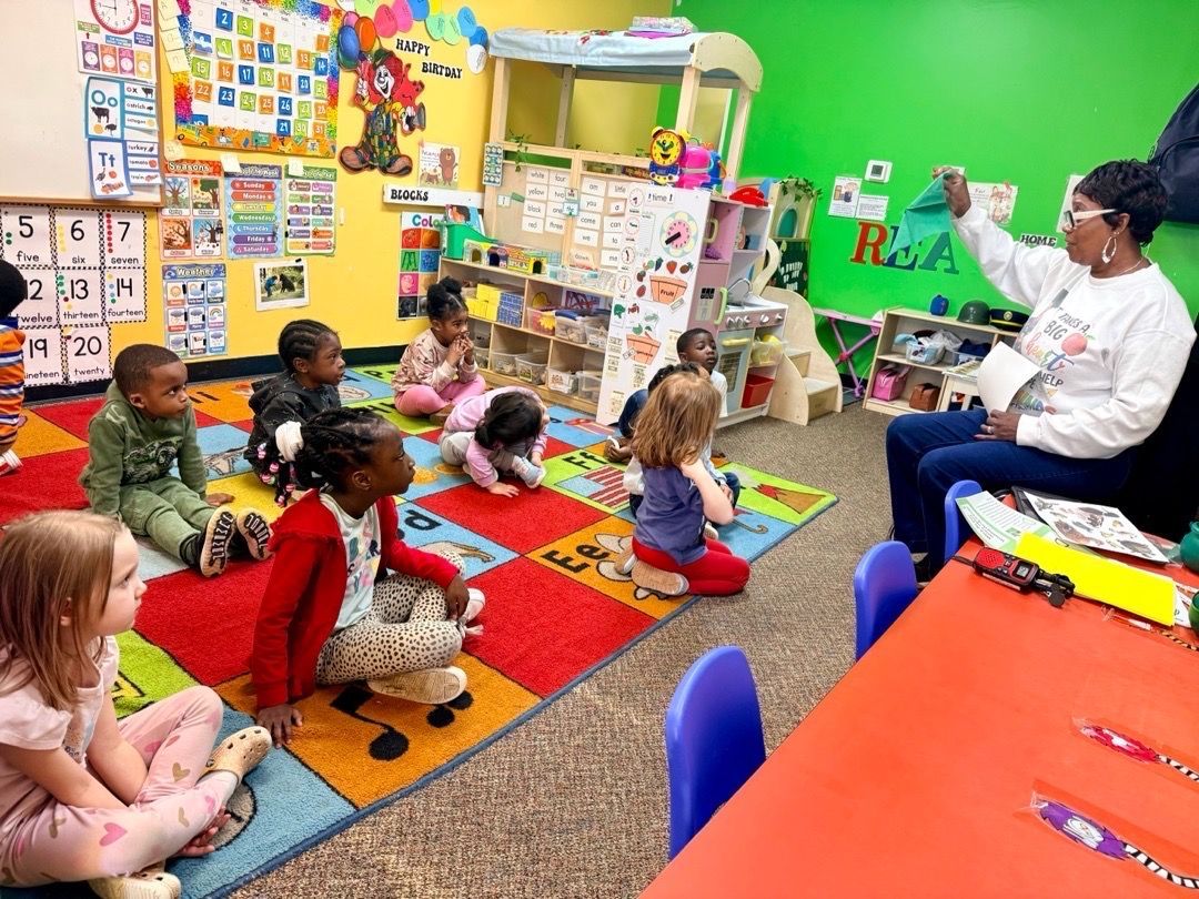 Group of children in blue shirts posing in front of a large airplane engine, with several adults.