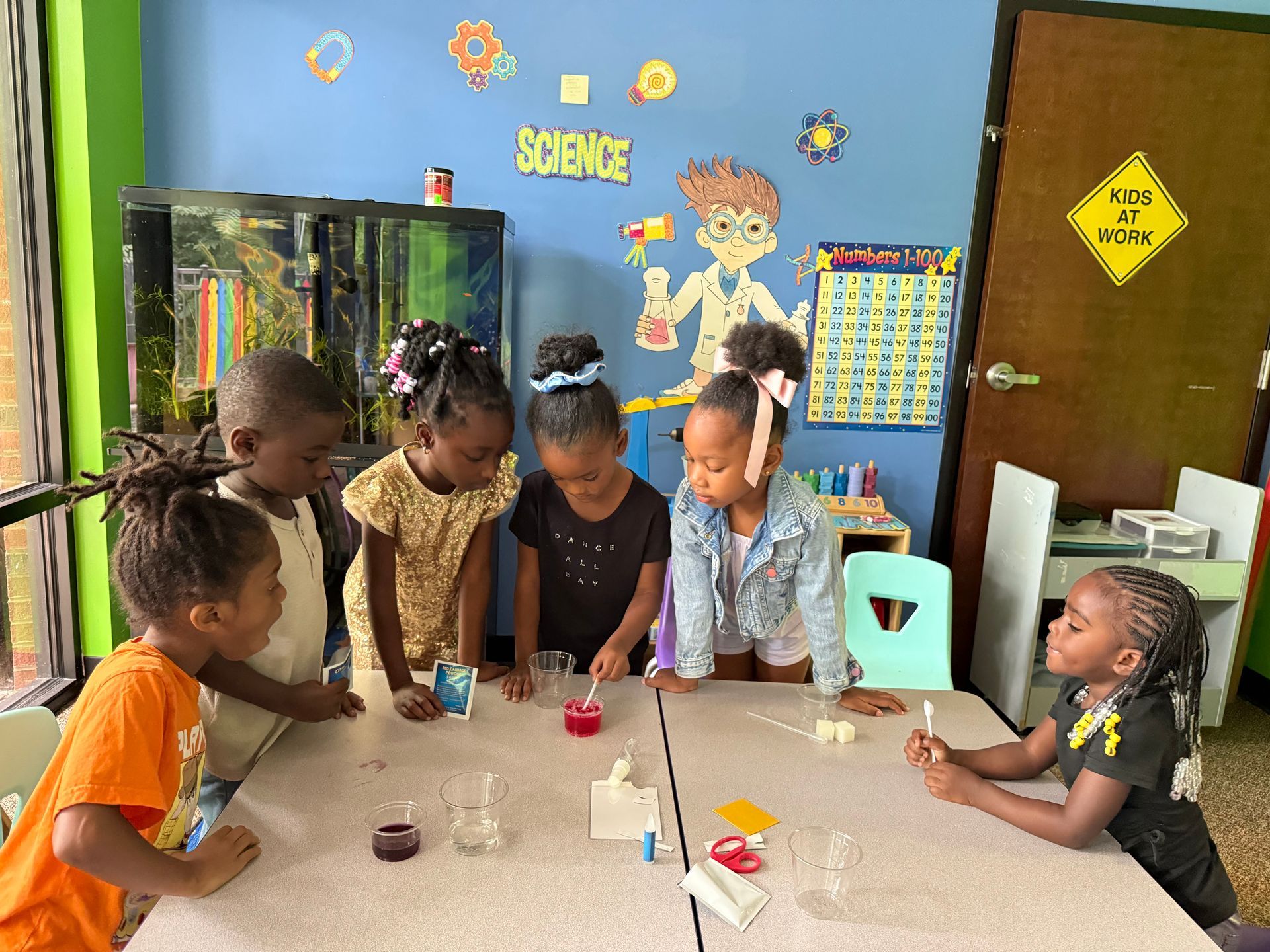 Children standing by white buckets in a sunny outdoor setting.