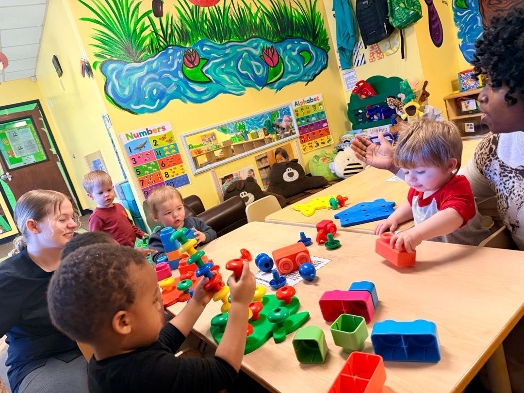 A group of children and an adult wearing colorful hats, smiling, and posing on a blue rug.