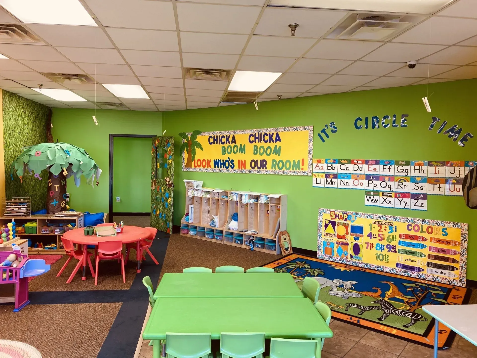 Children at a table create art with guidance from adults. Bright, colorful room.