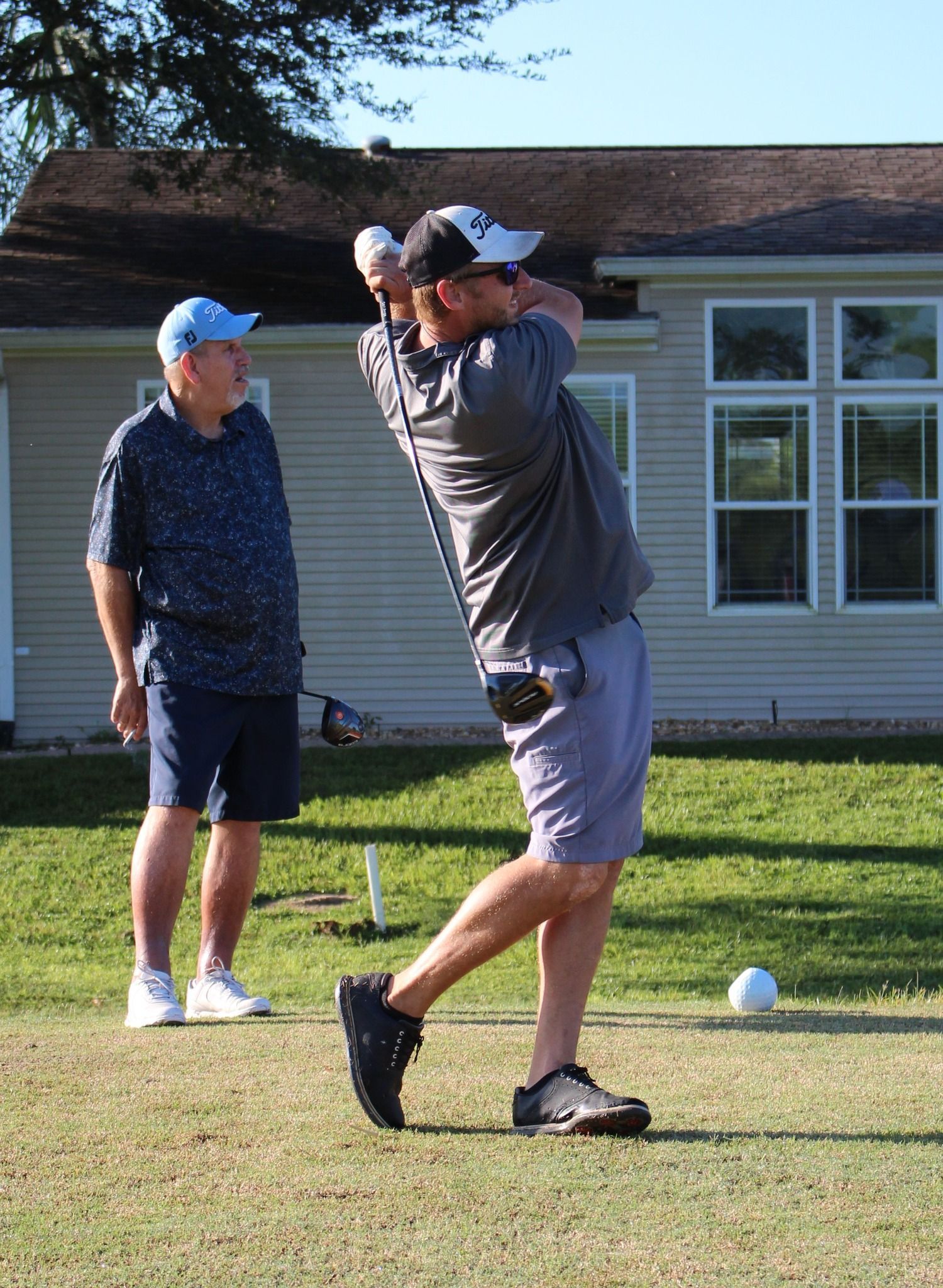 A man is swinging a golf club on a golf course while another man watches.