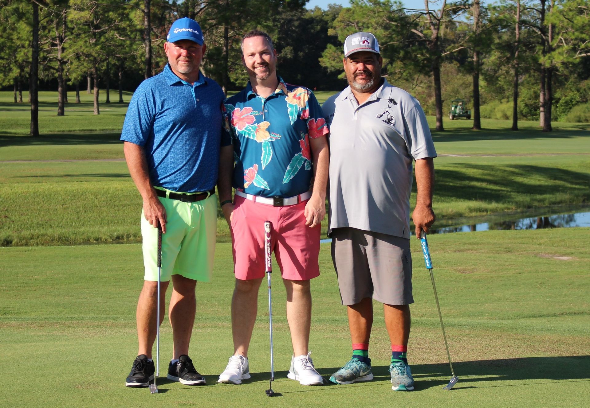 Three men are standing on a golf course holding golf clubs.