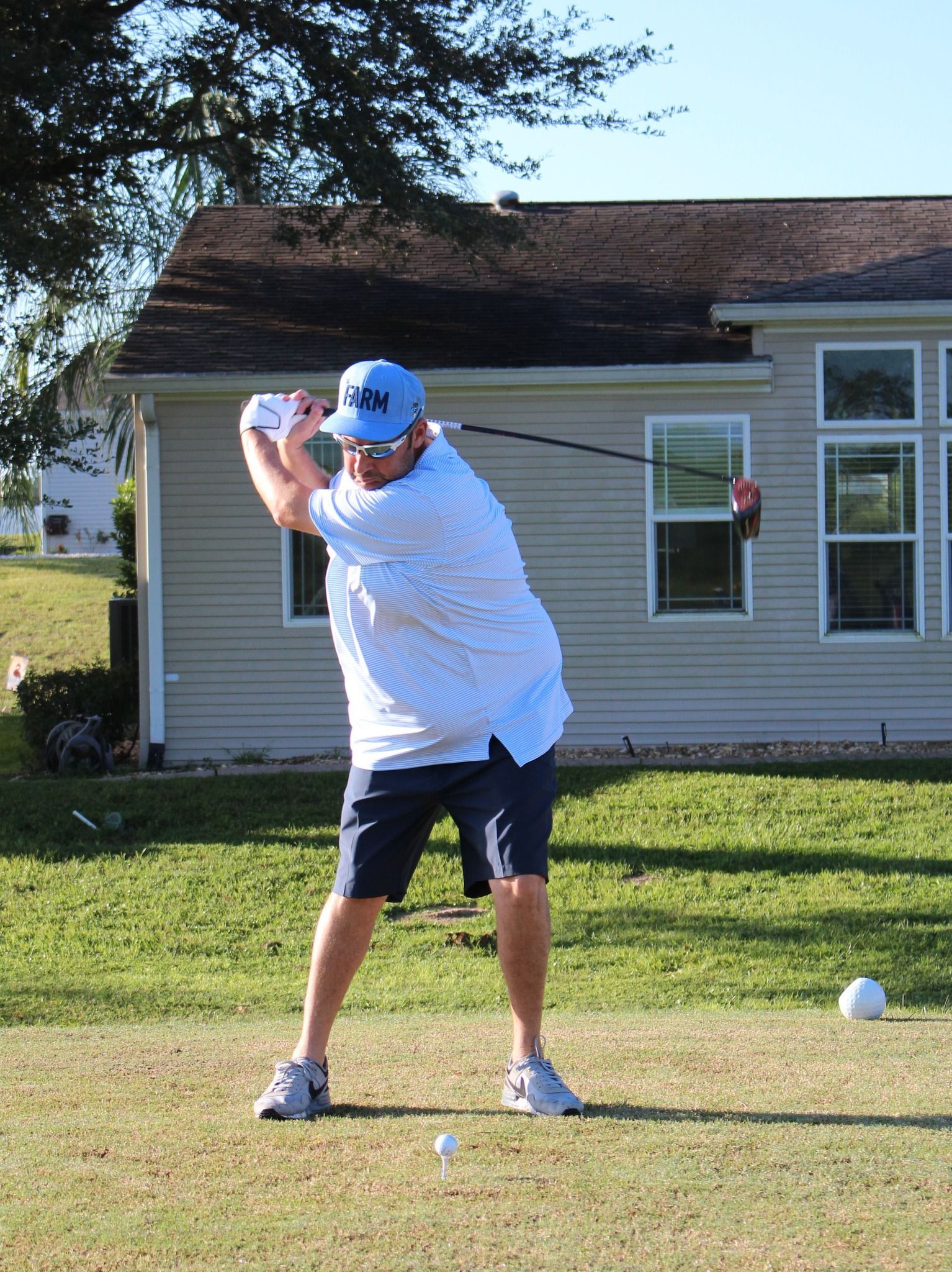 A man is swinging a golf club in front of a house
