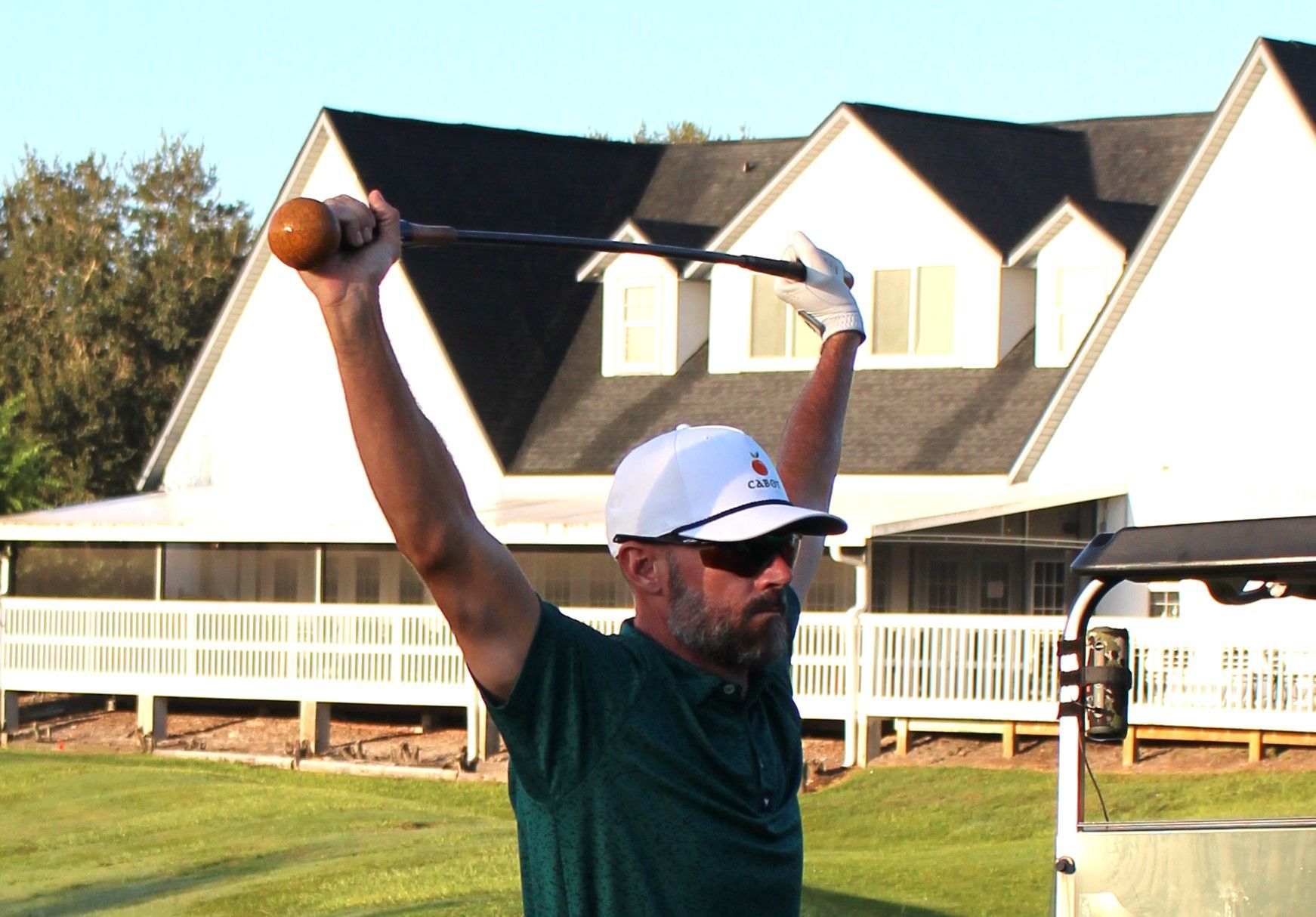 A man is holding a golf club over his head in front of a house