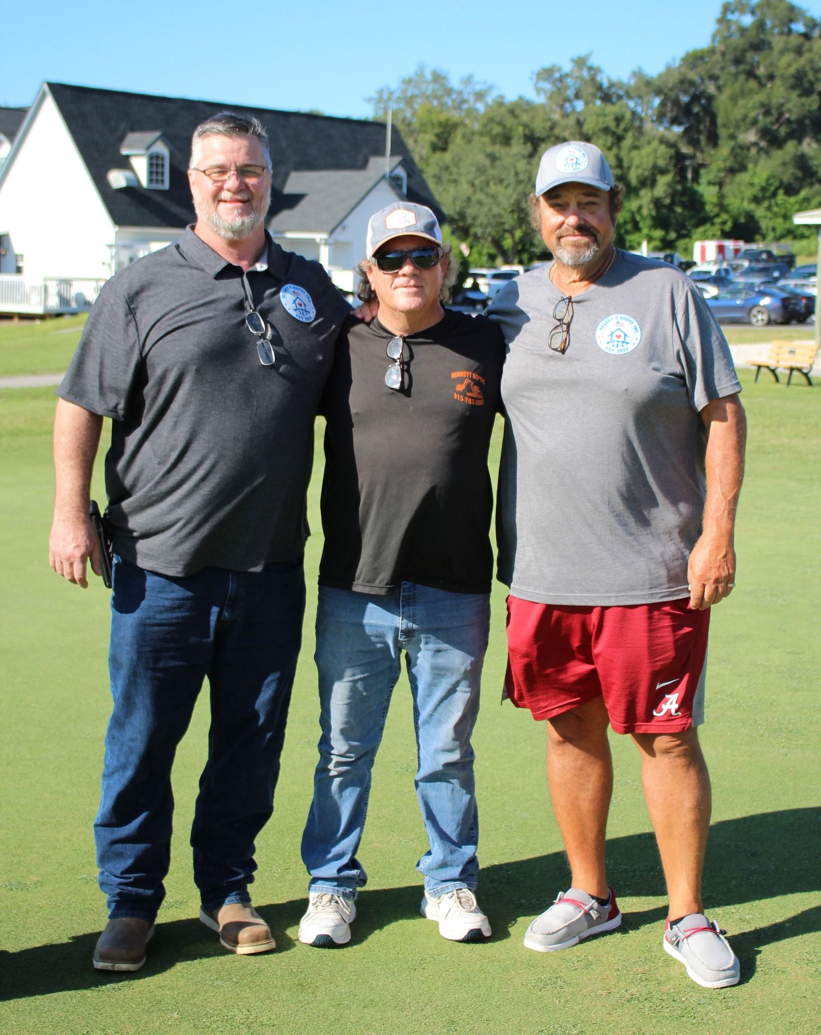 Three men are posing for a picture on a lush green field.