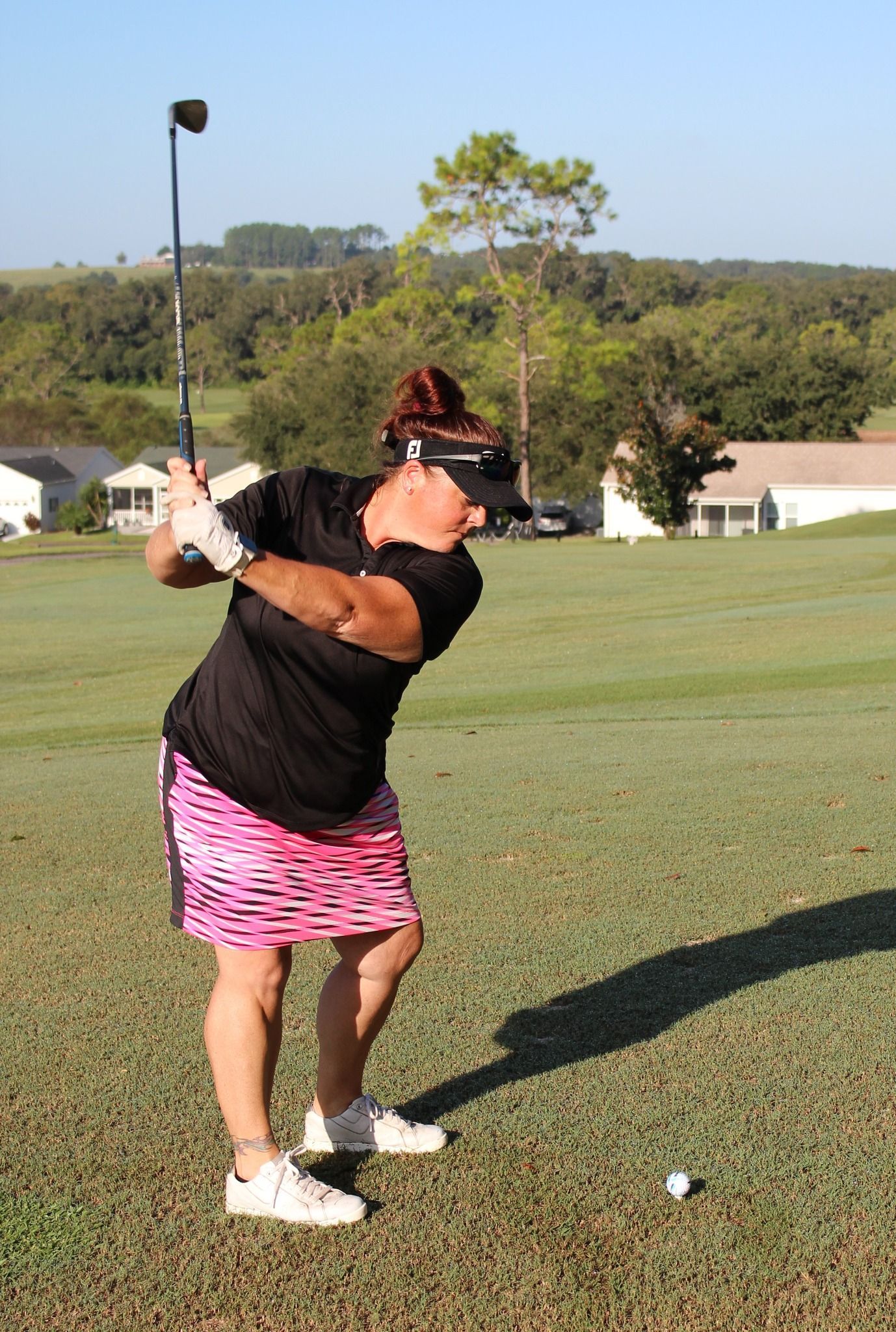 A woman is swinging a golf club on a golf course.