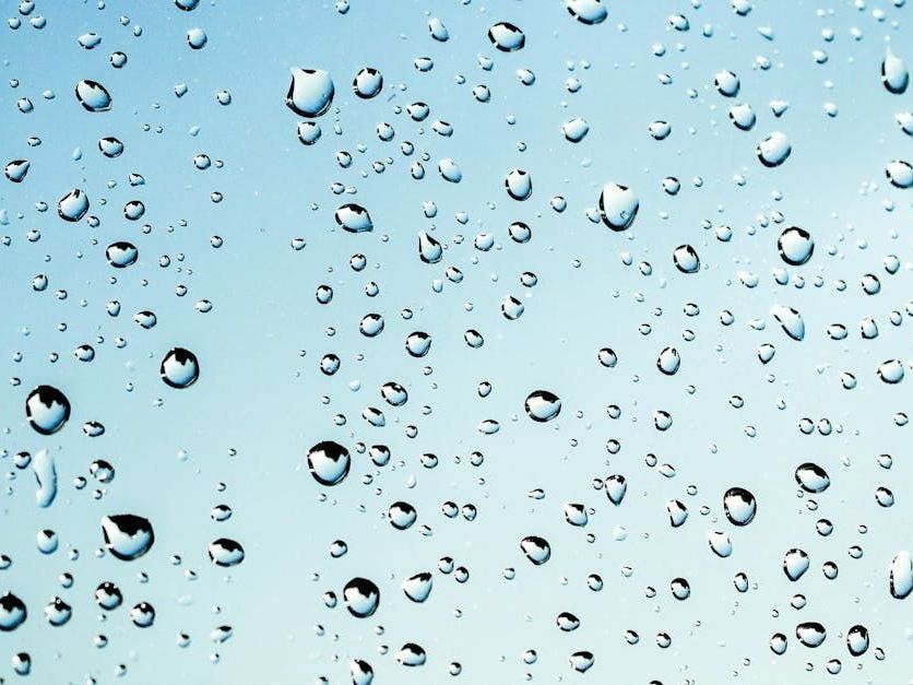 Water droplets on a clear glass surface, against a light blue background.