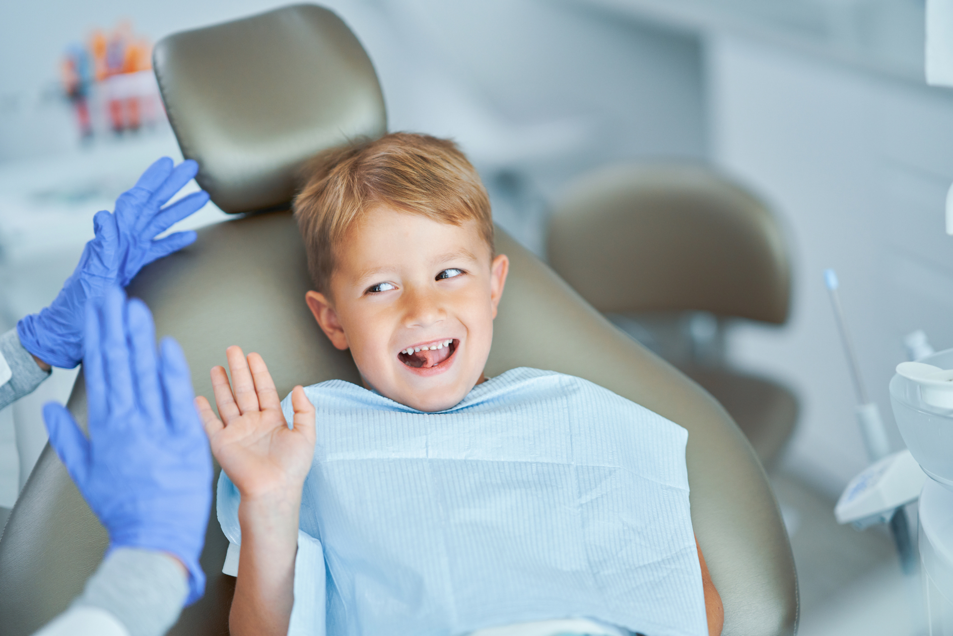 A young boy is sitting in a dental chair giving the dentist a high five.