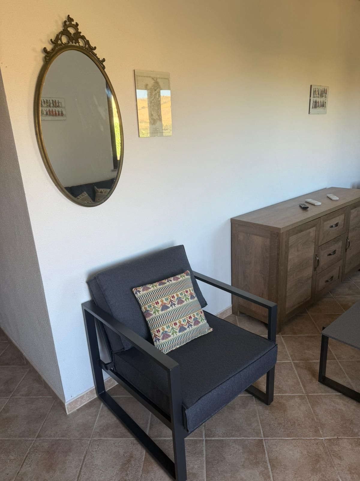 Stanza moderna con poltrona nera, specchio rotondo e credenza in legno su una parete bianca.